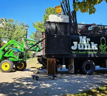 MrJunk® junk removal truck loading a mattress using a green tractor during a residential cleanout
